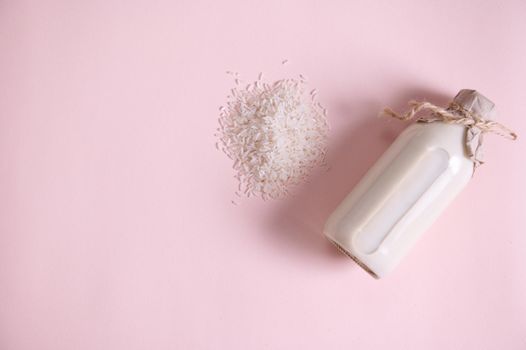 White rice, plant based, organic, raw vegan milk in a bottle, with kraft paper on the cap, tied with linen rope, isolated on a pink background. Copy the ad space. Healthy eating and veganism. Flat lay