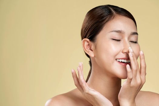 Closeup ardent girl with soft makeup applying moisturizing skincare cream on her face, isolated background. Skincare cream applied by female model concept.