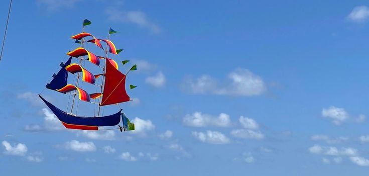 flying ship, rainbow colored ship kite flies on the blue sky and cloud in the beach