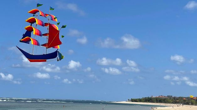 flying ship, rainbow colored ship kite flies on the blue sky and cloud in the beach