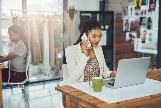 Shes business savvy. a fashion designer talking on her cellphone while using her laptop