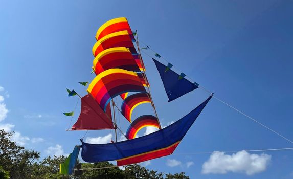 flying ship, rainbow colored ship kite flies on the blue sky and cloud in the beach