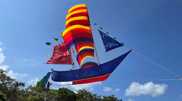 flying ship, rainbow colored ship kite flies on the blue sky and cloud in the beach