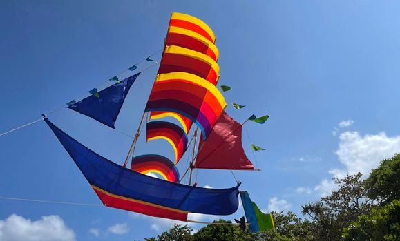 flying ship, rainbow colored ship kite flies on the blue sky and cloud in the beach