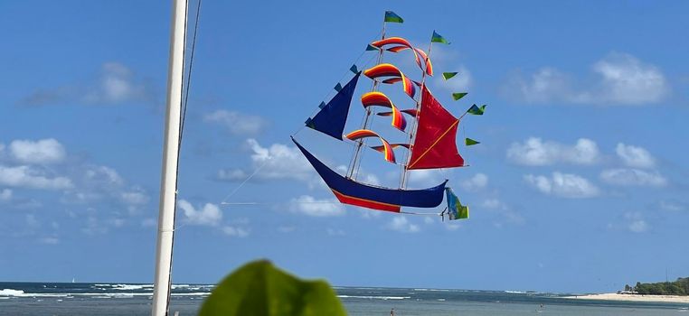 flying ship, rainbow colored ship kite flies on the blue sky and cloud in the beach