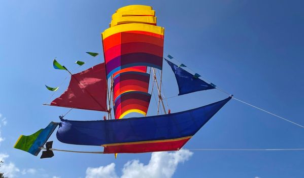 flying ship, rainbow colored ship kite flies on the blue sky and cloud in the beach