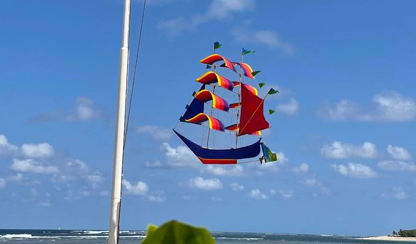 flying ship, rainbow colored ship kite flies on the blue sky and cloud in the beach