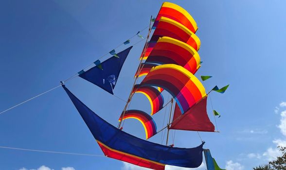 flying ship, rainbow colored ship kite flies on the blue sky and cloud in the beach