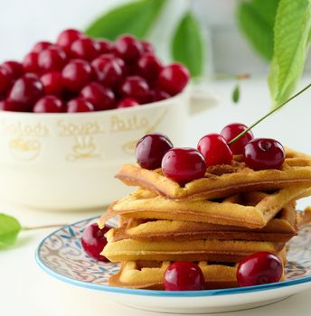 Stack of baked Belgian waffles with ripe red cherries, breakfast.	