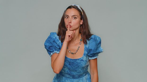 Shh be quiet please. Pretty young scared woman presses index finger to lips makes silence gesture sign do not tells secret. Adult stylish female girl isolated alone on gray studio background indoors
