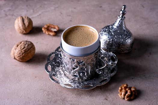 Small beautiful traditional cup with Turkish coffee stands on a beige background. Walnuts lie next to a coffee cup. Selective focus.