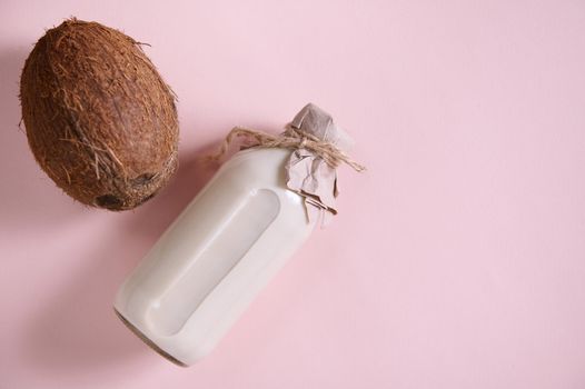 Flat lay. Still life with ripe organic raw vegan coconut and a bottle with wholesome alternative plant based, vegetable milk on a pink background with copy advertising space. Healthy food and drink