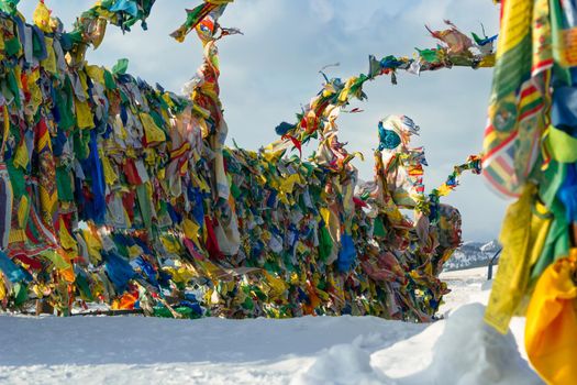 Lots of colorful traditional prayer flags with tibetan mantras hanging out in wind at snowy temple complex at cold winter, spiritual asian culture at local monastery, no people mountain landscape