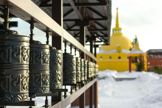 Rows of traditional copper-metal spinning prayer wheels with tibetan holy sacred mantras at snowy temple complex at winter, spiritual asian culture of Hindu and Buddhist faith at local monastery