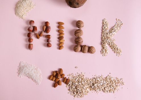 Flat lay. Lettering Milk using various nuts, cereals and seeds on pink background. Non dairy organic raw vegan healthy drink, made from rice, sesame, coconut, oats, almonds, walnuts and hazelnuts