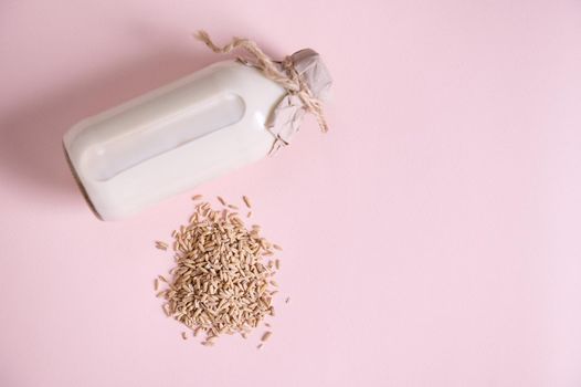 Flat lat. Still life with a heap of oat groats and glass bottle of plant based, organic, healthy oat milk, on pink surface with copy advertising text. Vegan wholesome dairy free drink. Healthy eating
