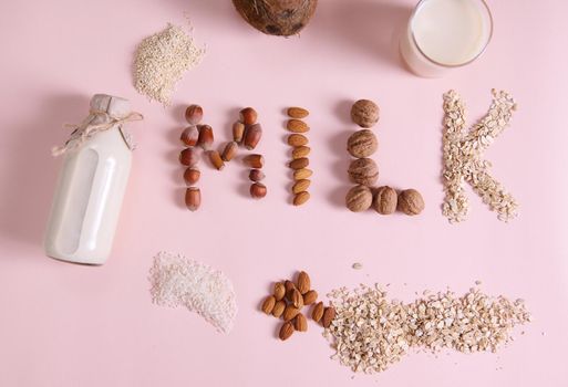 Flat lay Lettering Milk on pink background, using wholesome ingredients, cereals, nuts and seeds. Bottle of vegetable, alternative, dairy free milk made from White Rice Oatmeal sesame Almonds Coconut