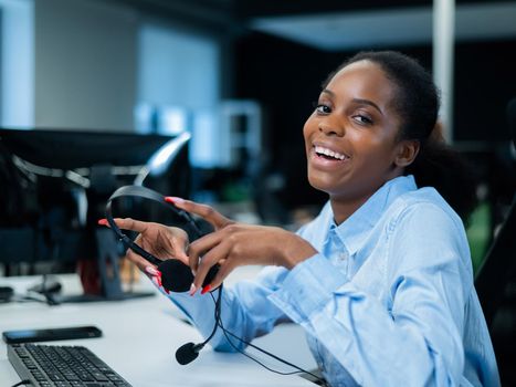 African young woman smiling and holding a headset in her hands. Call center employee
