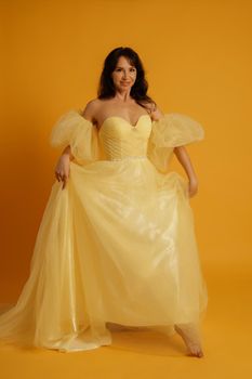 Portrait of a beautiful middle-aged woman in a yellow dress, her hair pulled up against a yellow background.