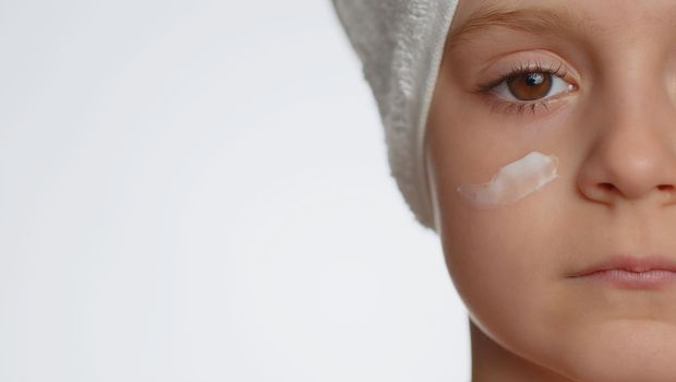 Close-up macro portrait of pretty young child girl applying cleansing moisturizing facial cream. Teenager kid face skincare healthy treatment, natural creme cosmetics. Perfect female fresh clean skin