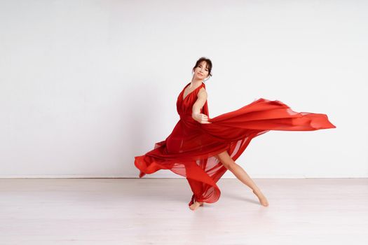 Dancer in a red flying dress. Woman ballerina dancing on a white studio background.