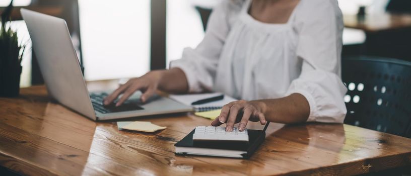 Business Accountant woman use calculator and computer with holding pen on desk in office. finance and accounting concept