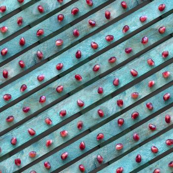 Red pomegranate seeds on a turquoise background. Diagonal line texture, top view. Contrasting colors.