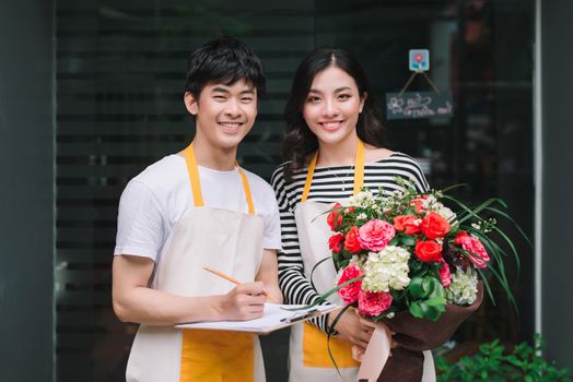 Two young handsome florists working at flowers shop. Looking at camera.