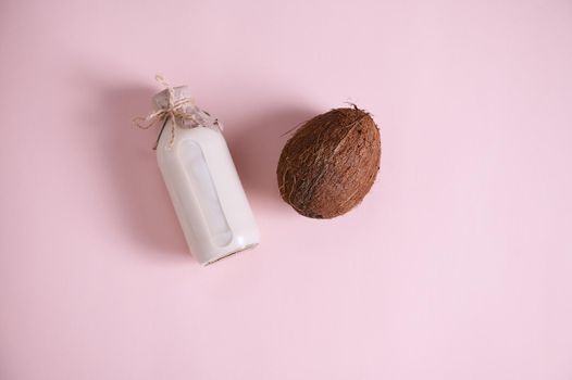 Flat lay composition with a bottle of a raw vegan, healthy organic plant based milk and a coconut, palm fruit isolated over pink background with copy space for advertising text