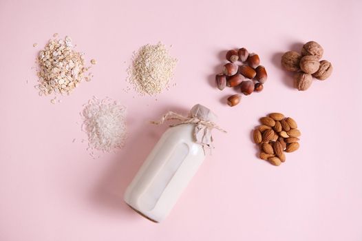 Flat lay. Still life with an assortment of wholesome organic seeds, nut, beans: almond, hazelnut, walnut, sesame, rice, oatmeal and a bottle with vegan plant based milk, isolated on pink background