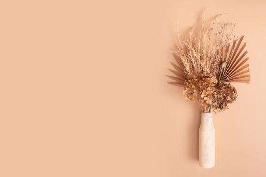 Bouquet of beige dried flowers, grass and leaves in a glass vase on beige background with copy space.