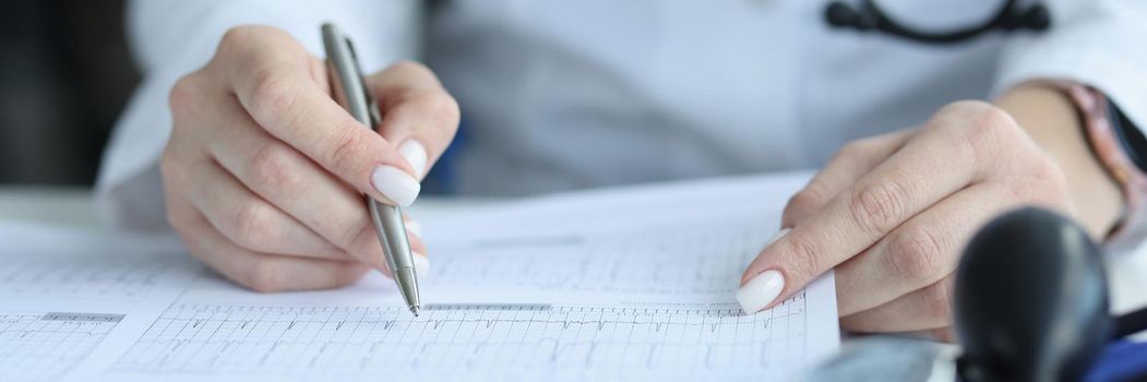 Doctor cardiologist examining patient cardiogram on paper in clinic closeup. Ecg diagnostics of rhythm and conduction disorders concept