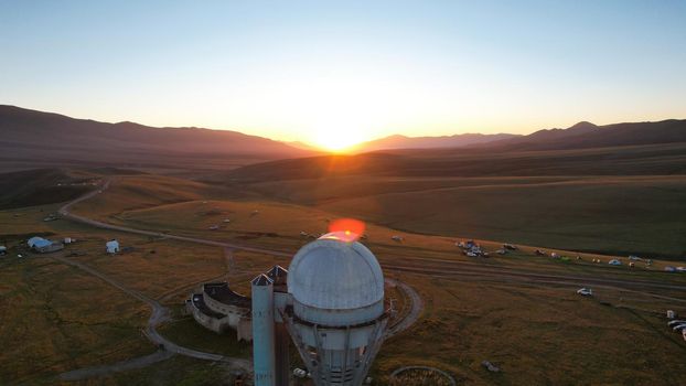 Bright dawn over the Assy-Turgen Observatory in the mountains. Aerial view from the drone of the camp of tents, cars and waking tourists. There is an old abandoned building. Kazakhstan, Almaty