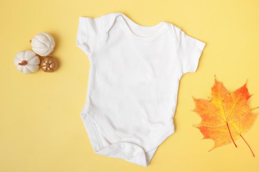 Baby clobodysuit mock-up top view with pumpkins and maple leaves on yellow background for your text or logo place in autumn season