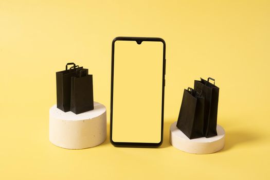 Phone mock up and black bags on podium with purchases in black friday sale on yellow background