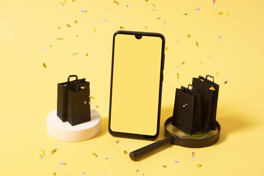Phone mock up and black bags on podium with purchases in black friday sale with sparkles on yellow background