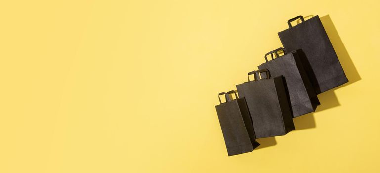 Black shopping bags on black friday sale yellow background with copy space. Banner format