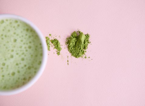 Selective focus on a japanese matcha powder, ground green tea near blurred white ceramic bowl with whipped antioxidant healthy drink- matcha latte with foam, over pink background with copy ad space