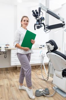 Smiling female dentist holding a clipboard with patient records in hands at dental clinic