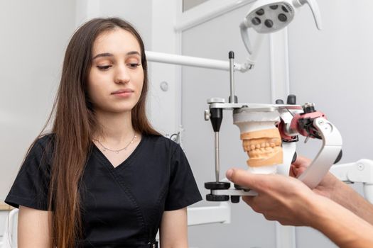 Dentist holding dental articulator with dental gypsum prosthesis model showing it to patient