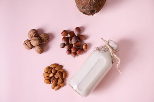 Still life with dairy free, plant based milk drink and organic wholesome ingredients, nuts: almonds, hazelnuts, walnuts and coconut for breakfast. Vegan food. Pink background. Copy space. Flat lay