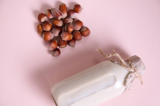 Flat lay with a vegetable milk in a glass bottle, alternative lactose free drink and a handful of organic wholesome hazelnuts on a pink background with advertising copy space. Selective focus