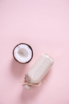 Vertical studio shot. Still life with with a half of coconut, lying next to a glass bottle with organic raw vegan plant based milk, isolated on pink background with copy space for advertising text.