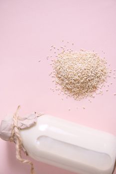 Selective focus. Still life with heap of white rice and glass bottle of plant based, organic, vegetable rice milk, on pink with copy advertising text. Vegan wholesome non dairy drink. Healthy eating