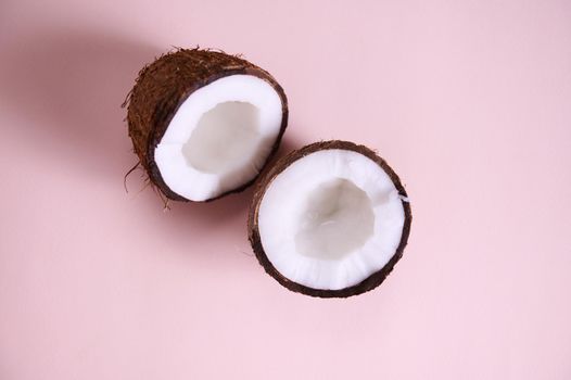 Flat lay. Still life. Two halves of ripe organic raw vegan coconuts, shot with soft shadow isolated on pink background with copy space for promotional text. Exotic tropical palm fruits. Healthy eating