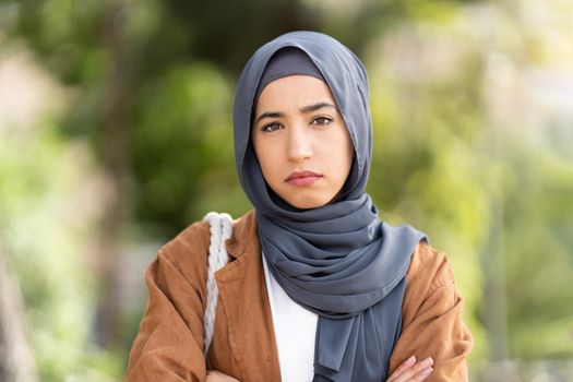 Muslim woman in a grey hijab crossing the arms while standing in the steet