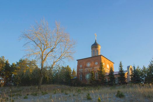 Orthodox church on a hill near the forest. Autumn sunset landscape with clear blue sky.