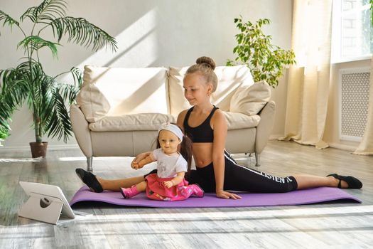 Little cute girl is practicing gymnastics at home. Video lesson. Kid repeating exercises while watching online yoga gymnastics session. Beautiful girl doing fitness exercise at home