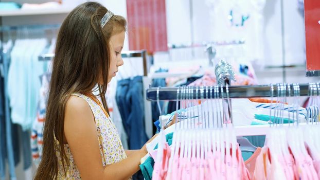 shopping in the store. children's clothing department. girl, kid, chooses things in the store. Little fashion-girl. little shopaholic. tedious shopping in stores, shops. High quality photo