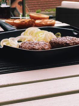 Cooking minced beef burger on cast iron grill skillet outdoors, red meat on frying pan, grilling food in the garden, English countryside living concept